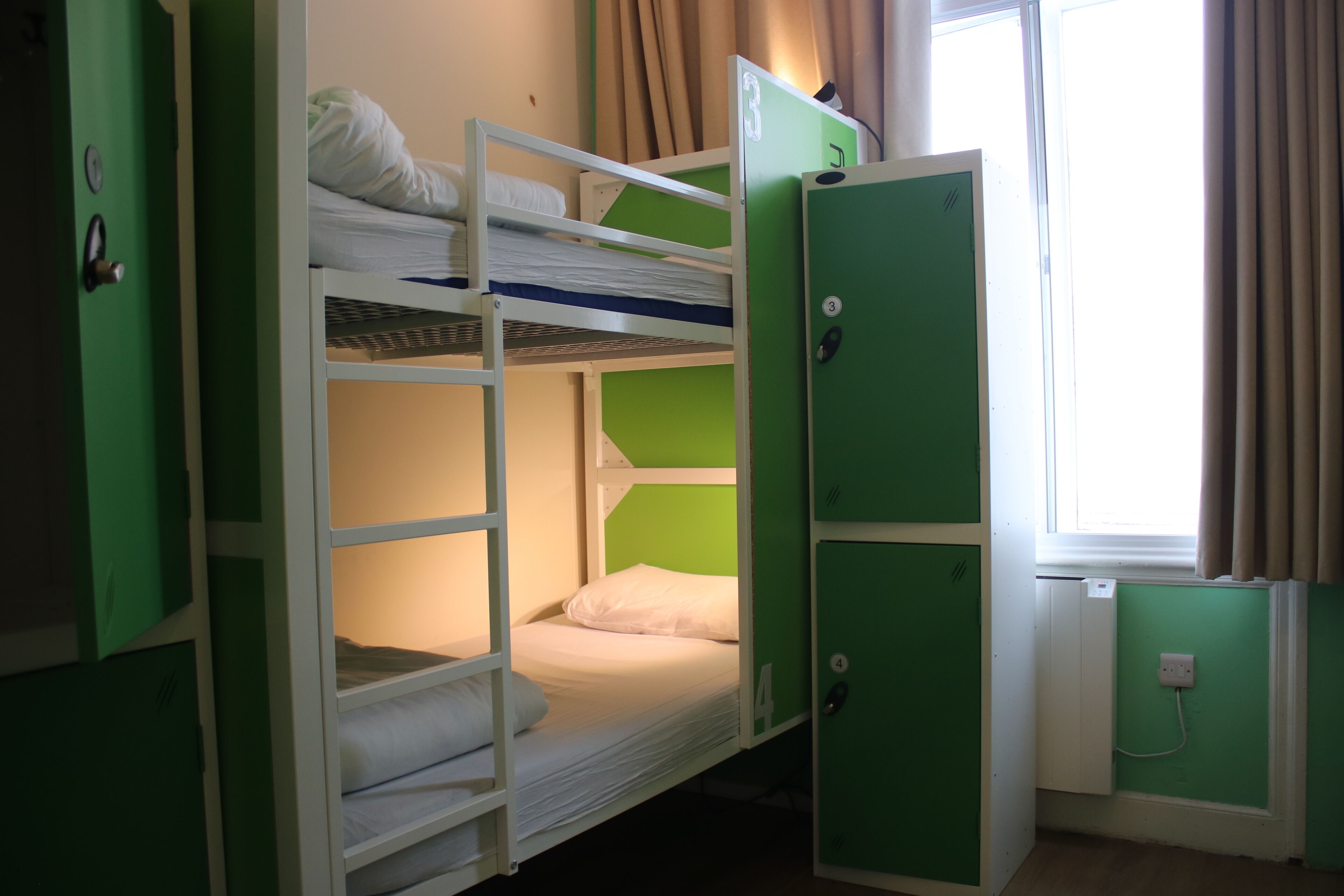 A bunk bed room with green lockers and a window with curtains.