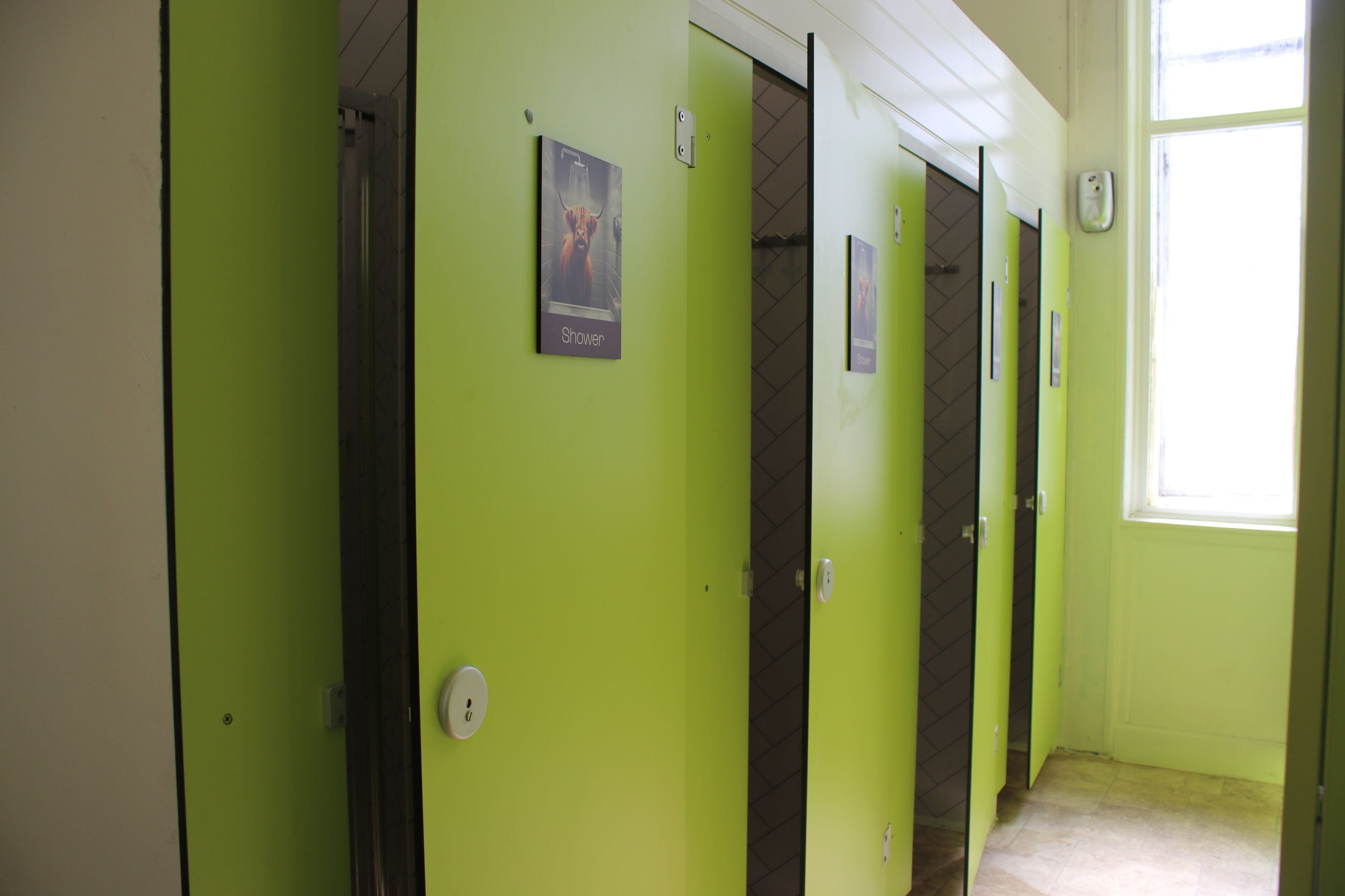 Una fila de cabinas de baño verdes con un cartel de ducha en la pared.
