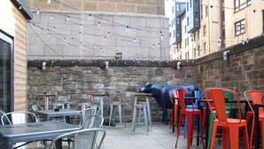 An outdoor patio area with tables and chairs, a stone wall, and a blue cow sculpture. - Safestay Edinburgh Cowgate (Edinburgh)