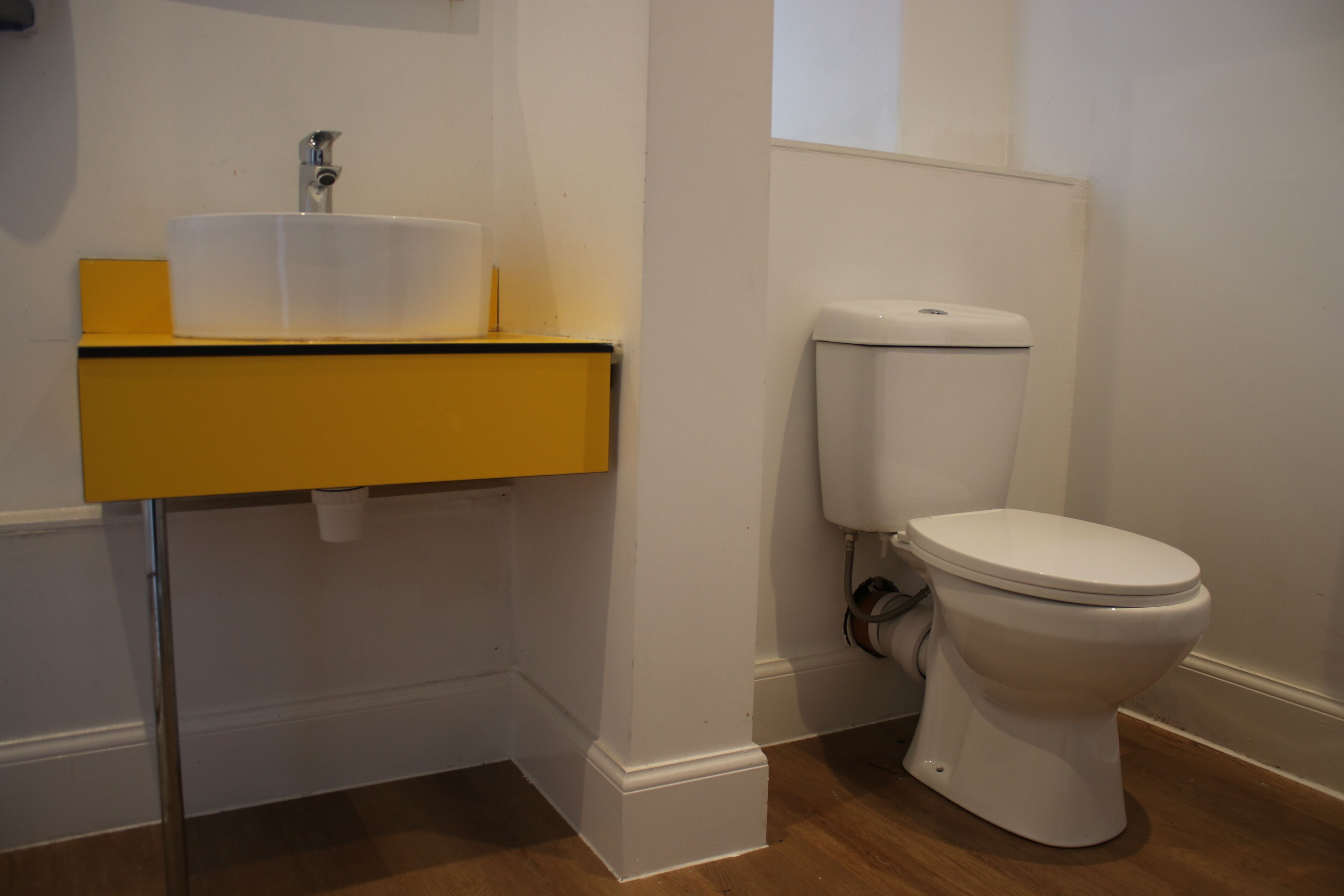 Une salle de bain avec des toilettes blanches, un lavabo jaune et un mur blanc.