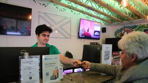 A reception desk with a digital screen displaying a music video, a store bag sign, and a QR code for store bags. - Safestay Edinburgh Cowgate (Edinburgh)