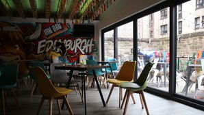 A restaurant interior with colorful chairs, a mural, and large windows offering a view of the street. - Safestay Edinburgh Cowgate (Edinburgh)