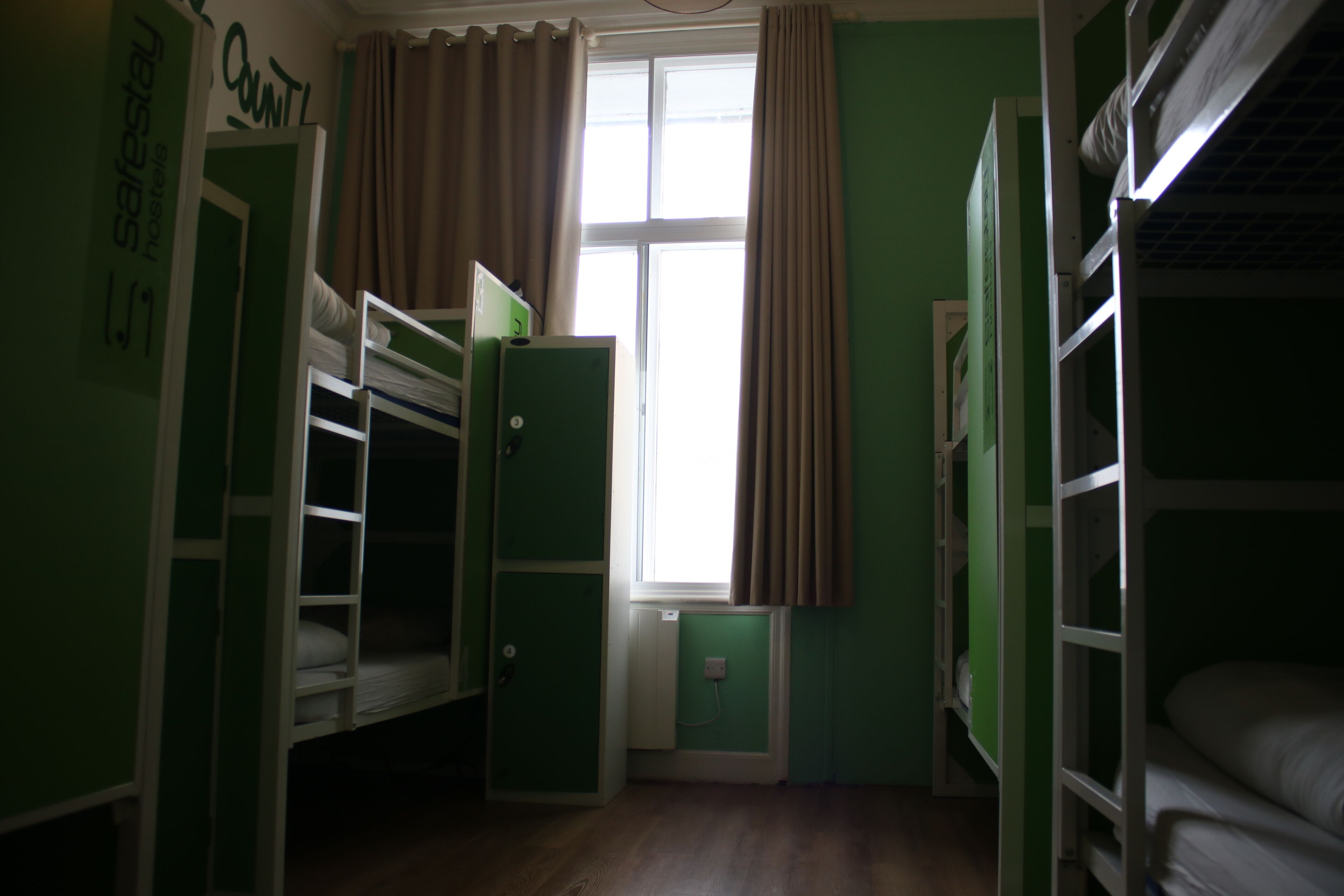 A dormitory room with bunk beds, a window with curtains, and a radiator.