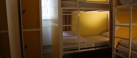 A bunk bed room with a wooden wardrobe and a window with curtains.