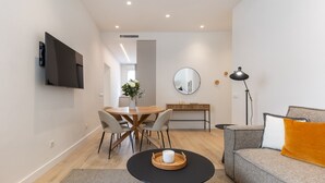Una sala de estar moderna con una mesa redonda de comedor, un sofá, un televisor montado en la pared y un escritorio con un espejo.