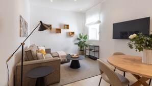 Una sala de estar moderna con sofá, mesa de centro y mesa de comedor. Hay estanterías, una planta y obras de arte en las paredes.