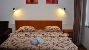 A neatly made bed with floral bedding, two wall-mounted lamps, and a heart-shaped painting above it. - Welcome&Enjoy King Studio 1 (Ohrid)