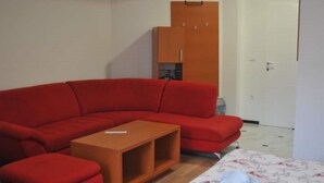 A red sectional sofa, a small wooden coffee table, a bed with a floral bedspread, and a wardrobe with a mirror. - Welcome&Enjoy King Studio 1 (Ohrid)