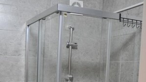 A glass-enclosed shower stall with a handheld showerhead and a fixed showerhead, a glass door, and a white sink to the right. - Welcome&Enjoy King Studio 1 (Ohrid)
