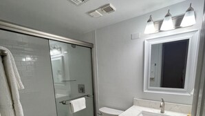 Ein modernes Badezimmer mit einer gläsernen Duschkabine, einer weißen Toilette und einem Waschtisch mit Spiegel und Waschbecken.