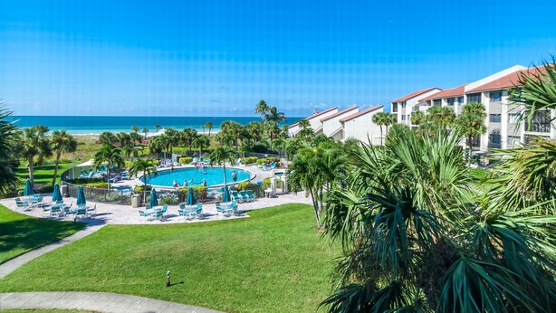 A pool area with lounge chairs and umbrellas, surrounded by palm trees and a view of the ocean. - Gorgeous Gulf views from this 2bd/2 bath condo (Sarasota)