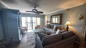 A living room with a ceiling fan, a sofa, a coffee table, and a view through a sliding glass door to an outdoor patio. - Gorgeous Gulf views from this 2bd/2 bath condo (Sarasota)