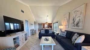 A living room with a TV, sofa, coffee table, and artwork. - Cathedral ceilings and incredible views in this 2Bed/2Bath Condo (Sarasota)