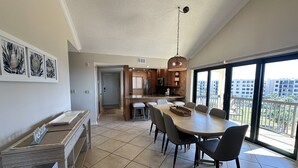 A spacious dining area with a large table and chairs, a kitchen in the background, and a balcony with a view of buildings. - Cathedral ceilings and incredible views in this 2Bed/2Bath Condo (Sarasota)
