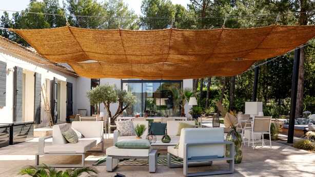 Eine Terrasse mit Gartenmöbeln, einem großen Sonnensegel und Blick auf die umliegende Bepflanzung.