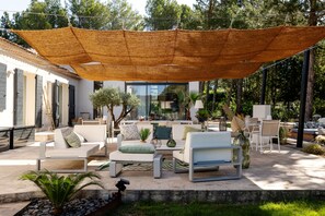 A patio with outdoor furniture, a large shade sail, and a view of the surrounding greenery.