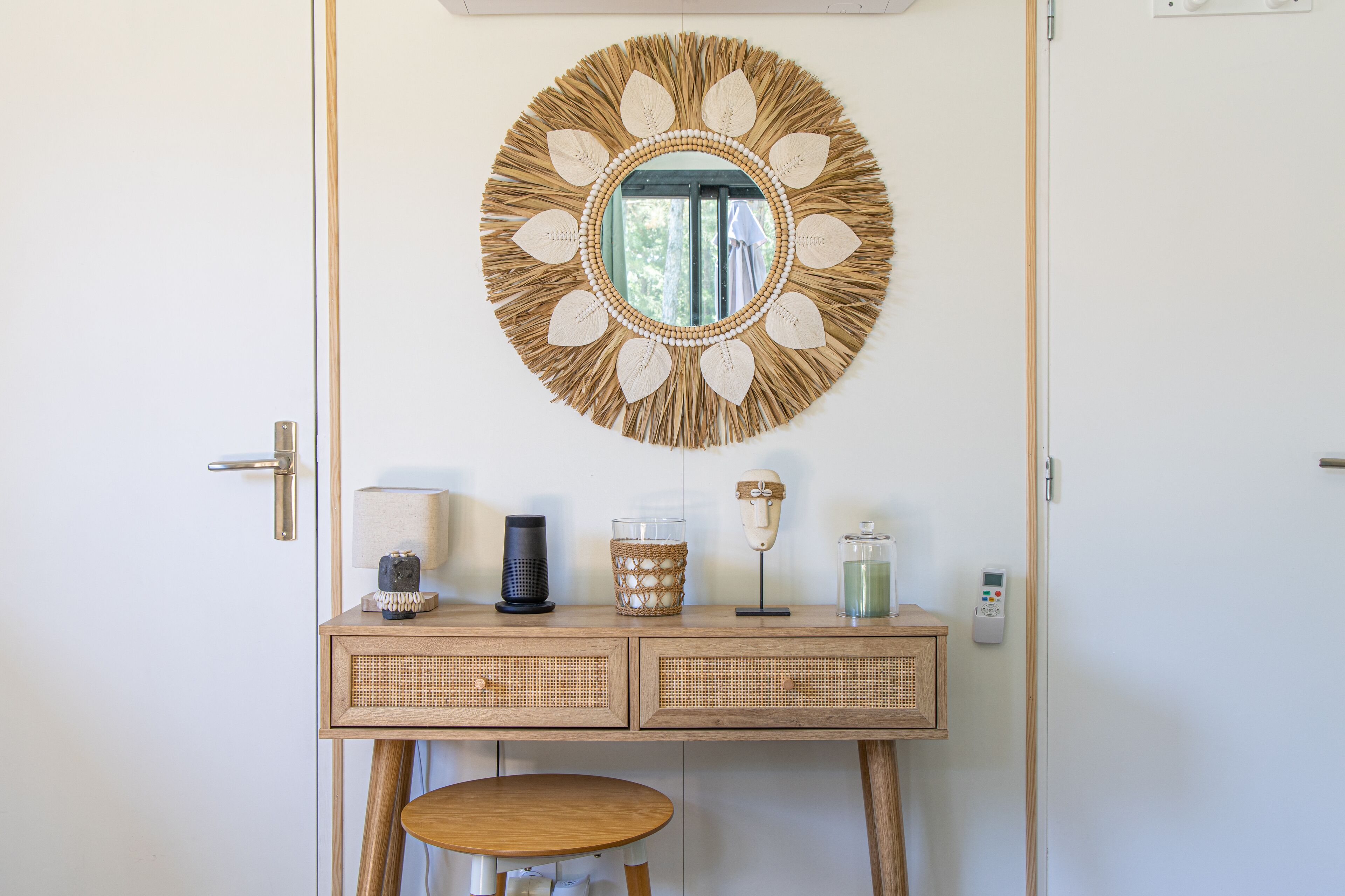 A room with a wooden vanity, a round mirror with a leaf design, and a small stool.