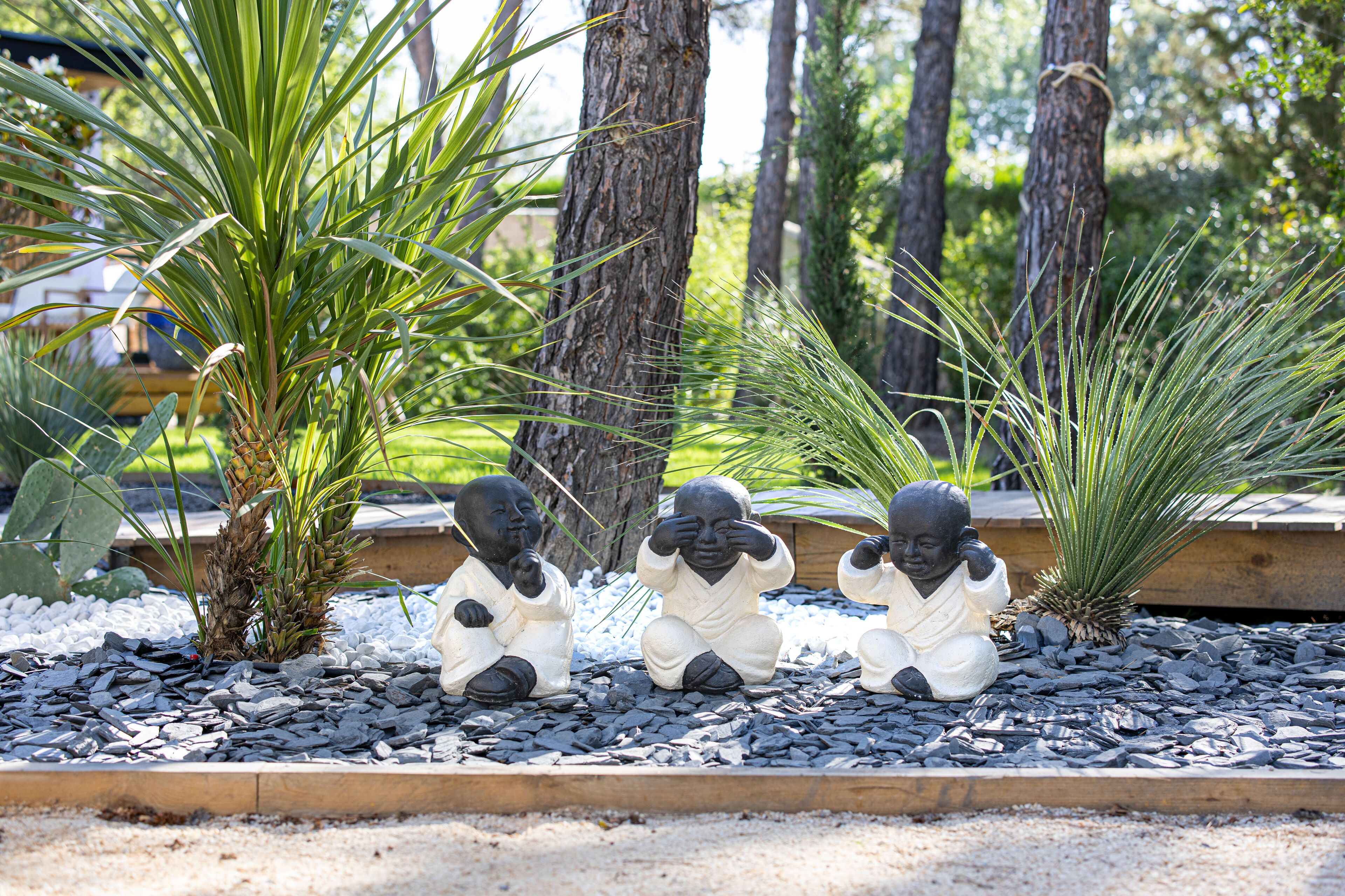 Tres estatuas de niños sentados sobre un lecho de rocas, con plantas de palmera al fondo.