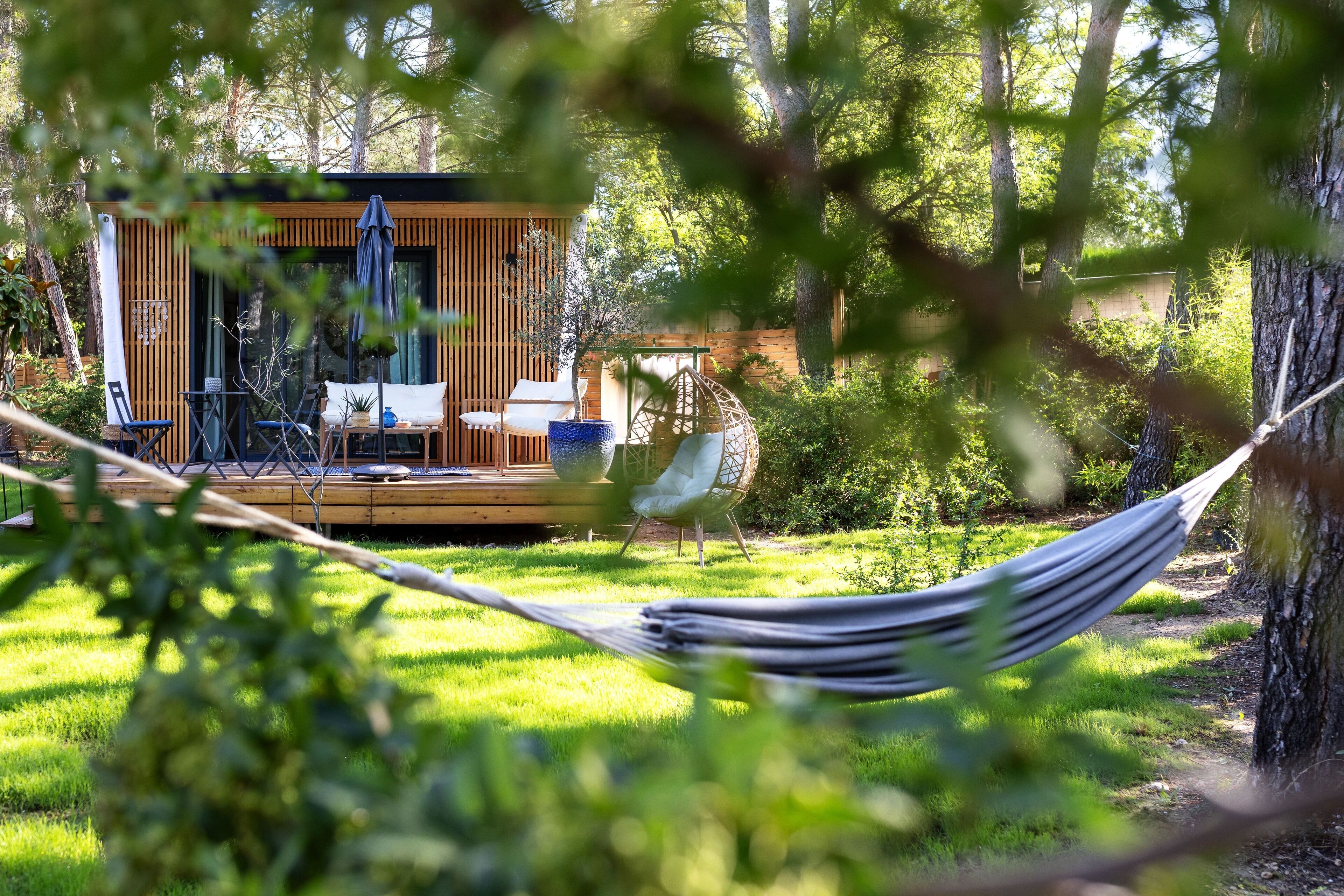 Une terrasse en bois, agréée de meubles d’extérieur, notamment des chaises et une table, et entourée d’une végétation luxuriante.