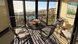Un balcon avec une table et des chaises, un ventilateur de plafond et une vue sur une piscine et des immeubles.