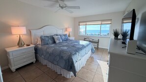 Une chambre à coucher comprenant un lit, des tables de chevet, un bureau, un ventilateur de plafond, une fenêtre avec vue et un téléviseur.