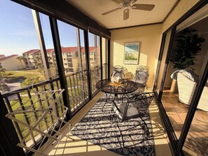 Un balcon avec une table et des chaises, un ventilateur de plafond et une vue sur les bâtiments et la verdure.