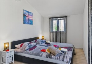 Una camera da letto con due letti, un comodino, una lampada, un quadro e una finestra con tende.