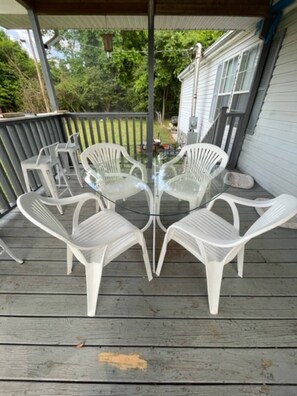 A covered outdoor patio with a glass-top table and four white plastic chairs. - Rainbows End River Lodge (South Pittsburg)
