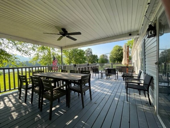 A covered outdoor patio with wooden flooring, tables, and chairs. - Rainbows End River Lodge (South Pittsburg)