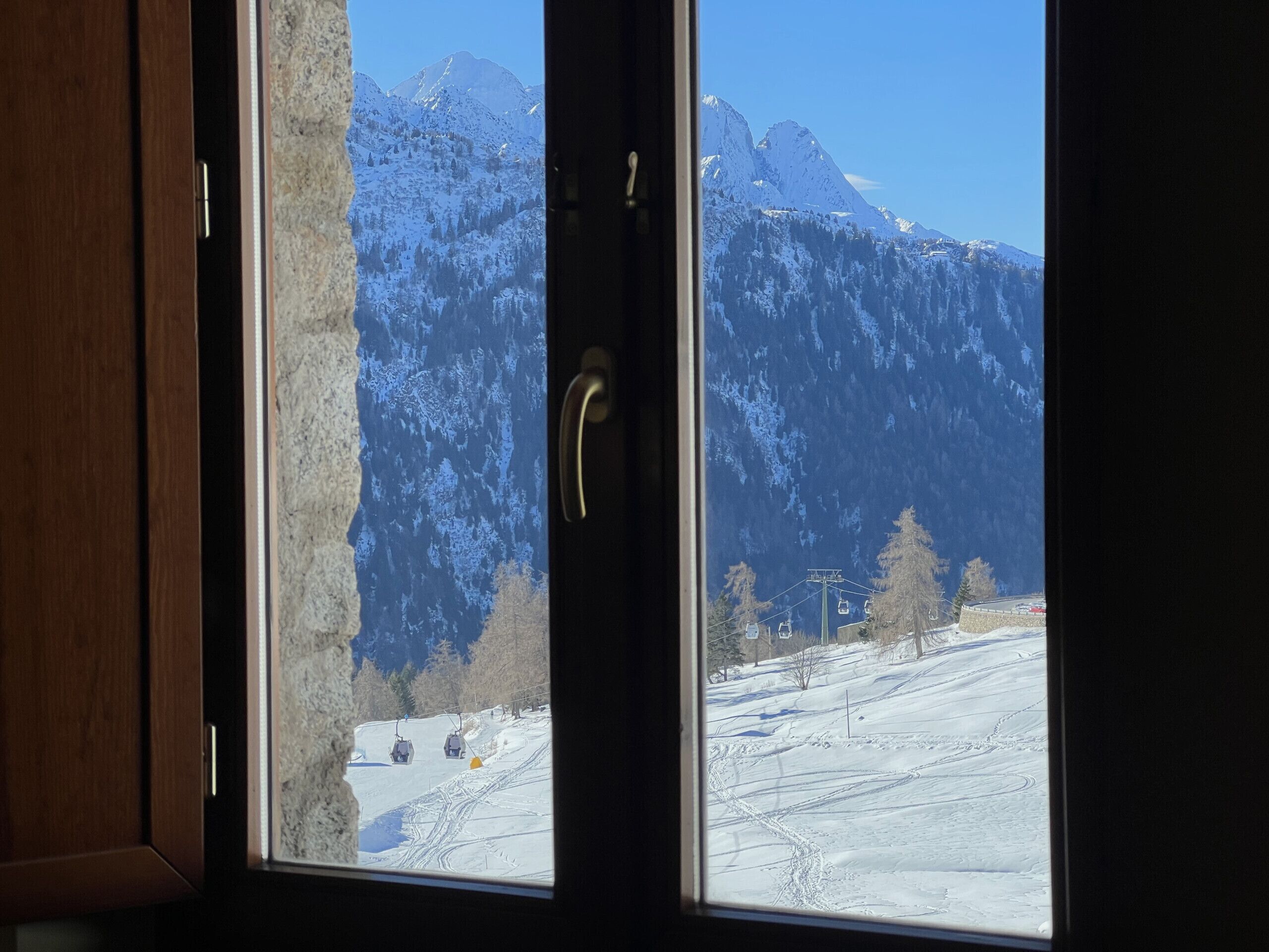 Aussicht aus einem Fenster auf eine verschneite Berglandschaft mit einer Seilbahn und einem Gebäude in der Ferne.