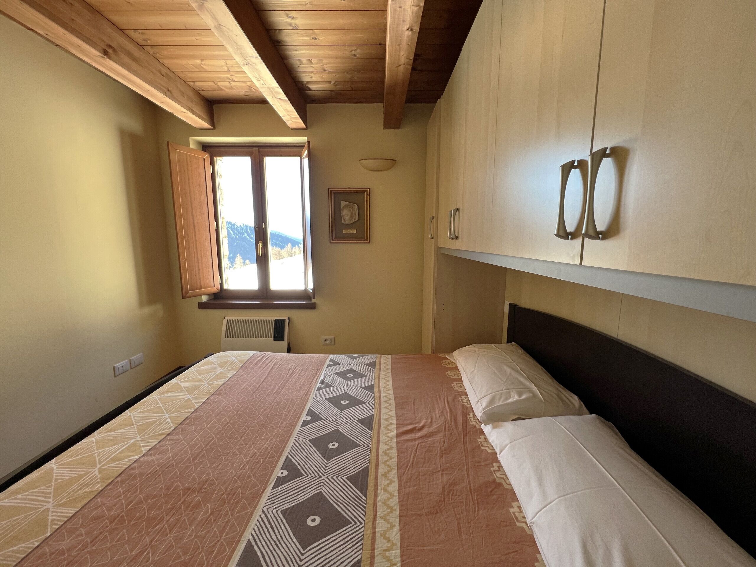 Une chambre à coucher avec un lit, des poutres en bois au plafond, une fenêtre donnant sur un beau paysage et un meuble fixé au mur.