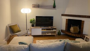 Ett vardagsrum med en platt-TV, en öppen spis, en soffa, en lampa och en hylla med dekorativa föremål.