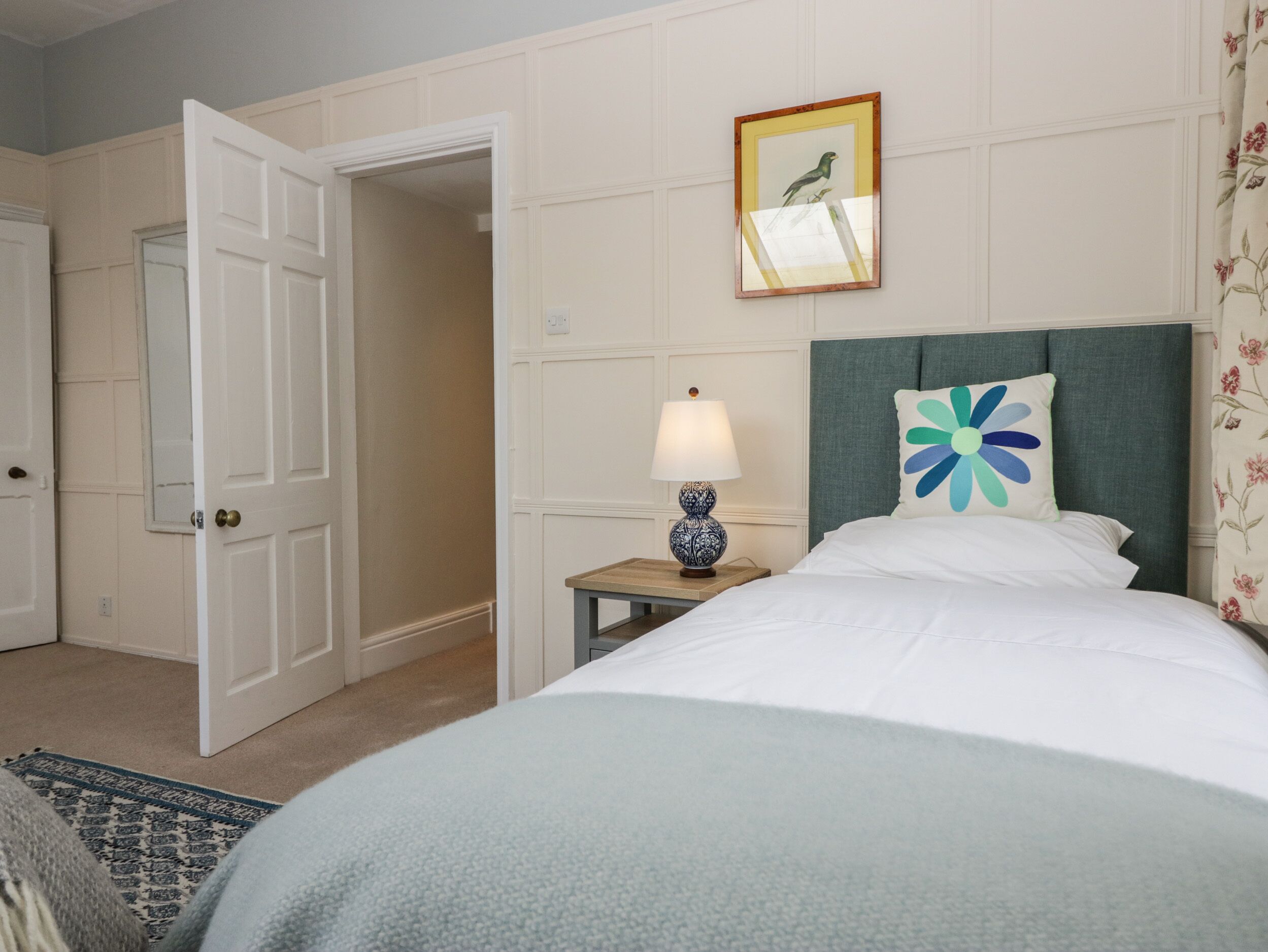 A hotel room with a bed, a nightstand with a lamp, a door, and a framed picture on the wall.