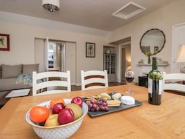 Una mesa de comedor con un bol de fruta, queso, galletas y una botella de vino.