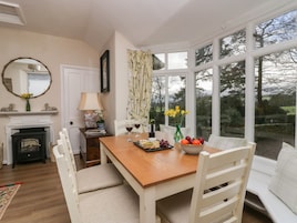 A dining area with a wooden table, white chairs, a fireplace, and a view of the outdoors through large windows.