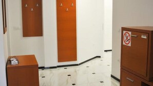 Um corredor com duas portas de madeira, um aviso de proibido fumar e uma pequena mesa com uma caixa.