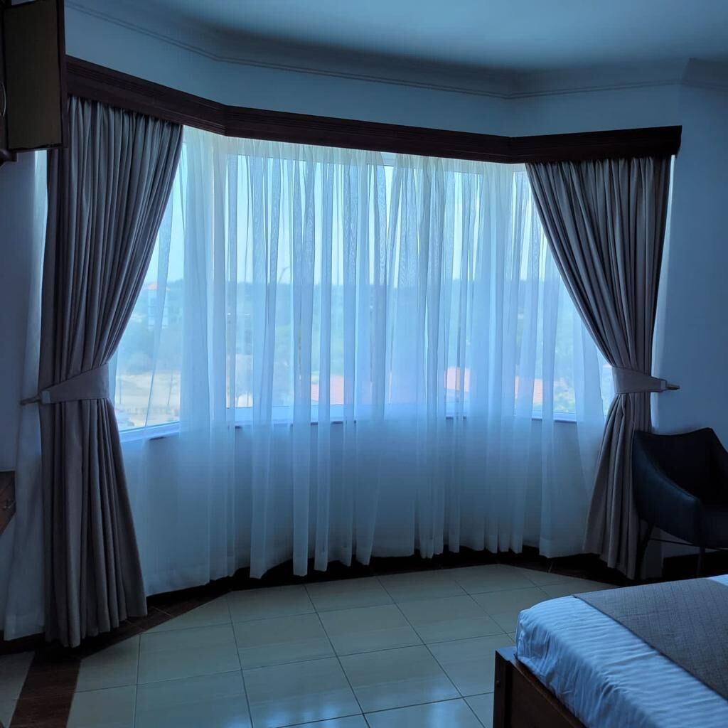 A hotel room with a large window, a bed, and a chair.