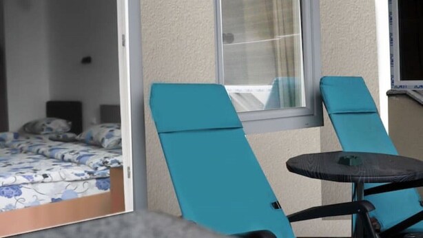 Huoneessa on sänky, ikkuna ja kaksi sinistä tuolia.