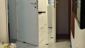 Un couloir étroit avec un lit sur la gauche, un distributeur d’eau et une porte fermée sur la droite.