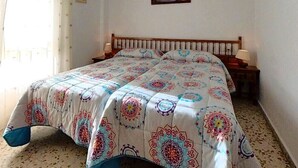 Un dormitorio con cama, mesita de noche, lámpara, un cuadro en la pared y ventana con cortinas.