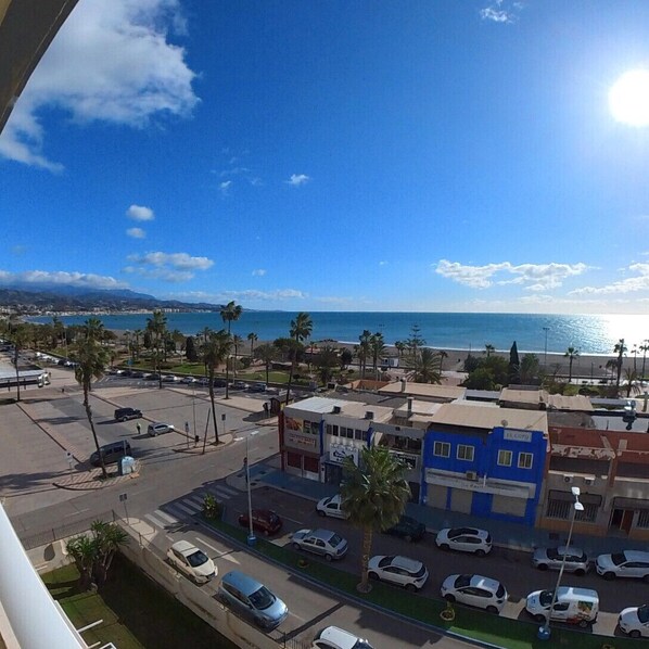 Un paisaje urbano costero con vista despejada al océano, palmeras y un estacionamiento con coches.