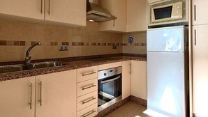 Una cocina con armarios color beige, un lavamanos de acero inoxidable, un horno empotrado y un microondas.