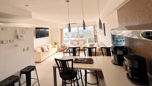 A modern kitchen with a dining area, large windows, and a water dispenser. - Sky Condo Tziara Panoramic View 8 Minutes From the Beach (Cancún)