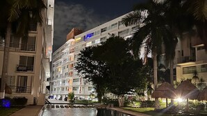 A nighttime view of a hotel pool area with a clear pool, lounge chairs, and palm trees. - Sky Condo Tziara Panoramic View 8 Minutes From the Beach (Cancún)