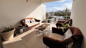 A balcony with a sofa, armchair, and potted plants. - Sky Condo Tziara Panoramic View 8 Minutes From the Beach (Cancún)