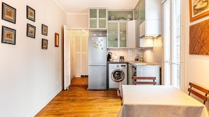 Eine kompakte Küche mit Waschmaschine, Kühlschrank und Essbereich inklusive Tisch und Stühlen.