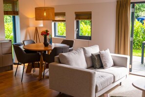 Relax in this serene living space with a sofa, dining table, and floor lamp, offering a view of lush greenery.