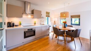 Una cocina moderna con una isla central, horno empotrado y una zona de comedor con una mesa redonda y sillas.