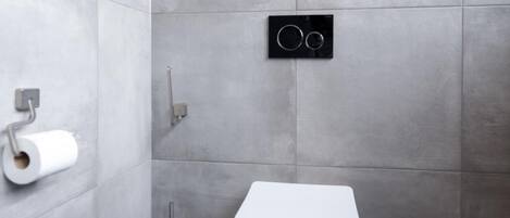 A modern bathroom with a toilet, a toilet paper holder, and a bidet.