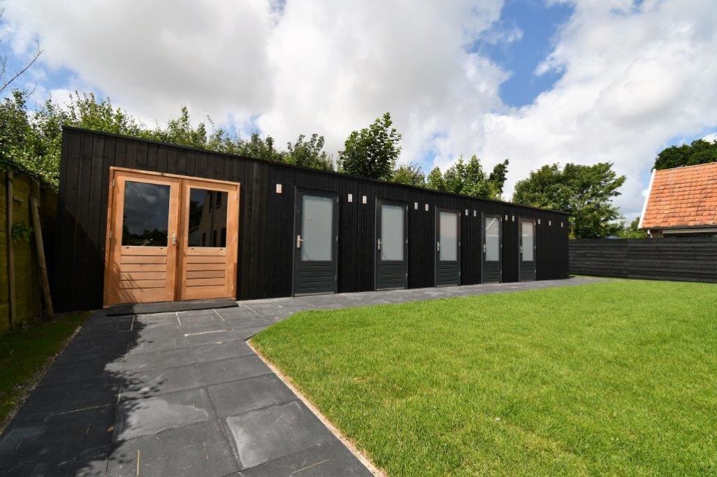 A modern building with a black exterior, a wooden door, and multiple windows.